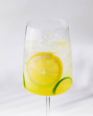 Limon ve limon dilimli bir bardak ferahlatıcı limonata beyaz bir küp üzerinde duruyor ve şık ve minimalist bir görünüm yaratıyor.