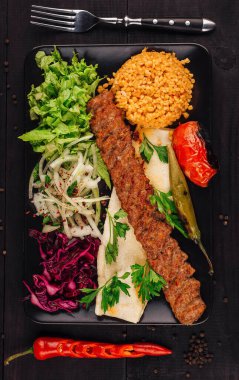 Lulah kebabı, yanında çatal ve taze sebzelerle birlikte siyah bir tabakta servis edilir.