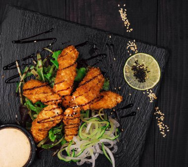 Lezzetli çıtır panko, siyah susam tohumlarıyla süslenmiş siyah taş tabakta servis edilen kızarmış karidesler.