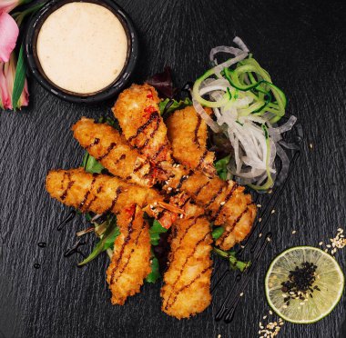 Yağda kızartılmış Kral karidesleri. Sos ve limon ile servis ediliyor. Siyah taş tabakta.