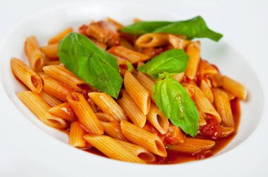Beyaz tabakta servis edilen taze fesleğen yapraklarıyla süslenmiş domates soslu lezzetli makarna.
