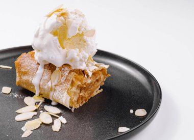 Elmalı turta, vanilyalı dondurma ve badem, modern siyah tabakta servis edilir.