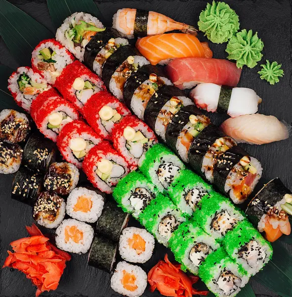 Farklı suşi ve rulo çeşitleriyle nefis suşi seti, siyah bir servis tahtasında wasabi ve zencefille süslenmiş.
