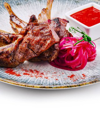 Izgara kuzu pirzolası, yanında soğan turşusu ve kırmızı sosla servis edilir.