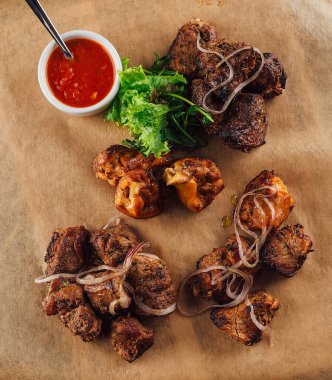 Taze otlarla süslenmiş çeşitli kesiklerden oluşan lezzetli bir tabak ızgara et ve yanında da baharatlı sos.