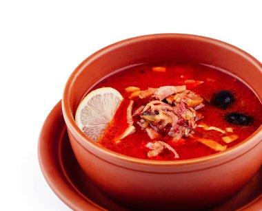 Beyaz arka planda kahverengi seramik kasede et, zeytin ve limonlu Solyanka çorbası.