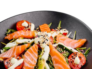 Avokado, kiraz domatesli somon salatası ve susam tohumlu roka ve siyah tabakta sos.