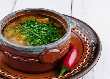Geleneksel bir kasede servis edilen maydanozlu Ukrayna çorbası ve yanında beyaz ahşap bir masada kırmızı biber.