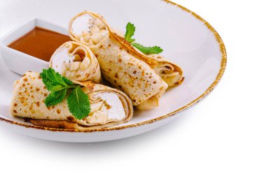 Süzme peynirli ince krepler ve nane yapraklarıyla süslenmiş muz dilimleri beyaz tabakta tatlı soslu.