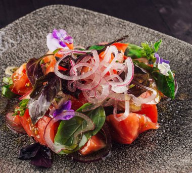 Domatesli taze ve sağlıklı salata, kırmızı soğan ve zeytin yağıyla tatlandırılmış fesleğen ve yenilebilir çiçeklerle süslenmiş.