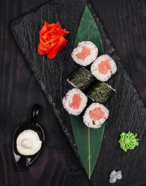 Siyah taş tabakta ton balıklı lezzetli suşi ruloları zencefil, wasabi ve mayonez ile servis ediliyor.