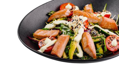 Taze ve sağlıklı salata, somon, domates, roka ve kremalı sos beyaz arka planda siyah bir kasede servis edilir.
