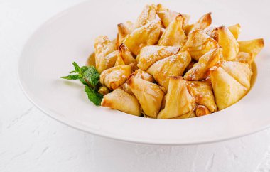 Nane yaprağıyla süslenmiş lezzetli elmalı krepler, temiz beyaz bir arka planda servis ediliyor.