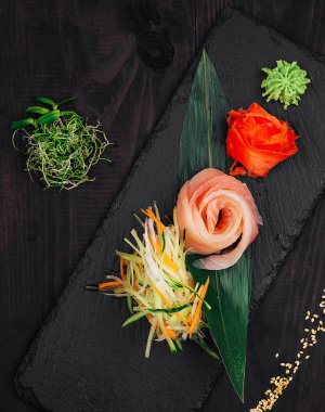 Taze somon balığı, siyah bir tabakta wasabi, zencefil ve sebze ile servis edilir.