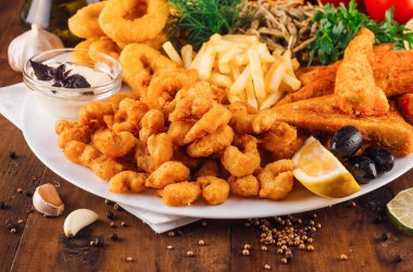 Ahşap masada patates kızartması servis edilen büyük bir tabak lezzetli deniz ürünü.