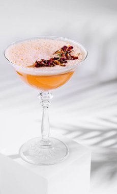 Beyaz küpün üzerinde duran çiçek yapraklarıyla süslenmiş köpüklü içecekle süslenmiş zarif bir kokteyl bardağı.