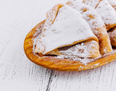 Beyaz masadaki ahşap tabakta duran pudra şekerli nefis ev yapımı krepler.