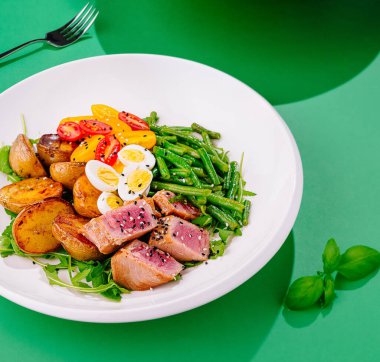 Nicoise salad with seared tuna, green beans, potatoes, eggs, and tomatoes on a white plate clipart