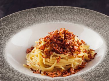 Peynir soslu spagetti ve güzel bir restoran ortamında servis edilen kızarmış pastırma parçaları.