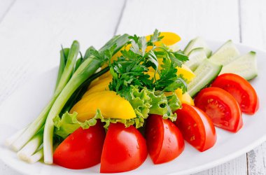 Dilimlenmiş domatesler, salatalıklar, biberler ve yeşil soğanlar beyaz bir tabakta sıralanarak renkli ve sağlıklı bir yemek oluştururlar.