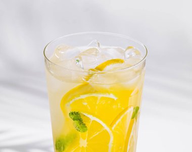 Buzlu uzun bir bardak limonata, limon dilimleri ve beyaz arka planda naneli.