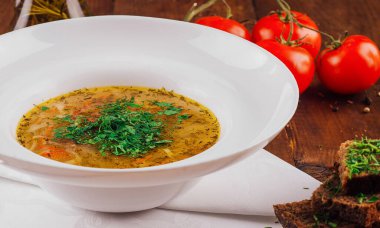 Ekmek ve domateslerle birlikte beyaz bir kasede servis edilen otlu tavuk çorbası.