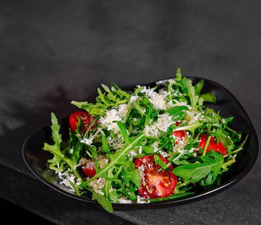 Lezzetli domatesli ve traşlı parmesan peynirli canlı roka salatası, şık bir siyah tabakta servis edilir.