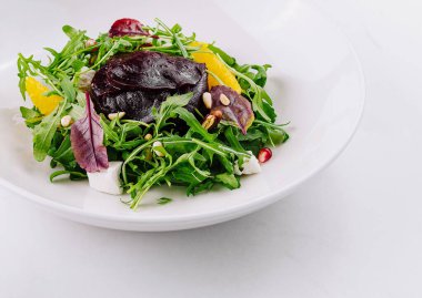 Canlı bir tabak karışık yeşillik, otlar ve beyaz arka planlı narenciye.