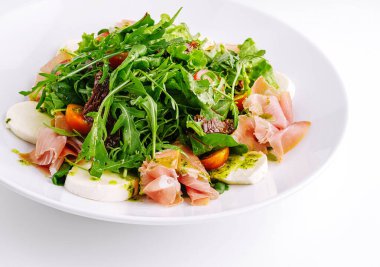İçinde prosciutto, mozzarella peyniri ve roka bulunan taze salata lezzetli ve görsel olarak çekici bir yemek yaratır.