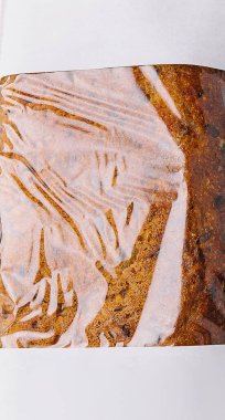 Plastik filme sarılı taze pişmiş ekmek pastası iştah açıcı dokusunu ve altın rengi kahverengi rengini gözler önüne seriyor.