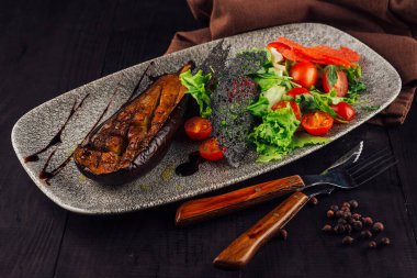 Izgara patlıcan taze domates, marul ve bitkilerle servis edilir. Gri bir tabakta, biber ve balzamik jöleli.