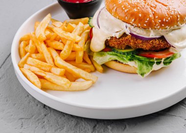 Beyaz tabakta patates kızartması ve soslu lezzetli bir tavuk burgerinin yakın çekimi.