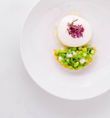 Beyaz bir tabakta sunulan gurme aperatifi kremalı bir krema ve taze sebzeli tart sunuyor.