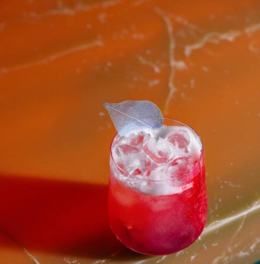 Red cocktail with ice and silver leaf garnish standing on a bar countertop clipart