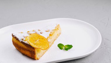 Çekici bir dilim portakallı pasta toz şekerle kaplanmış, bir dilim portakal ve nane ile süslenmiş.