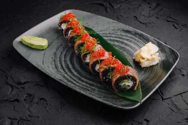 Parlak kırmızı havyarla kaplanmış renkli suşi ruloları parlak siyah bir tabakta ustalıkla düzenlenir. Wasabi ve turşulu zencefil eşliğinde, mutfak yaratıcılığı sergileniyor..