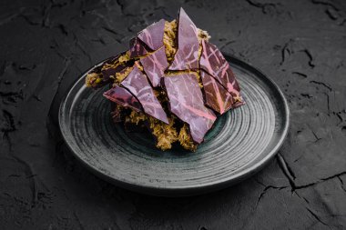 Katmanlı, çarpıcı mor ve kahverengi desenli güzel düzenlenmiş bir tatlı koyu, desenli bir tabakta oturur. Çağdaş sunum tatlının eşsiz tasarımını vurguluyor..