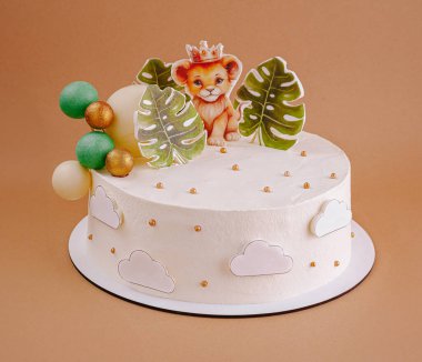 Güzel tasarlanmış bir doğum günü pastasında, tropikal yapraklar ve renkli kürelerle çevrili, tacı olan oyuncu bir aslan bulunur. Orman temalı bir kutlama için mükemmel..
