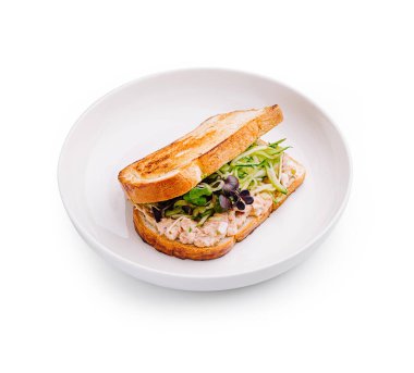 Kızarmış bir sandviç beyaz bir tabakta sunulur, şeffaf tavuk salatası katmanları, çıtır yeşiller ve narin filizler sergilenir. Yemek ya da atıştırmalık için mükemmel bir seçim..