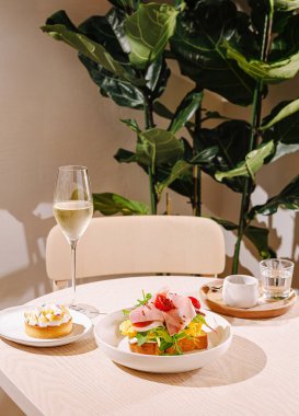 Güzel düzenlenmiş bir masa, üzerine jambon ve bir bardak köpüklü içeceğin yanında tatlı bir hamur işi ile renkli bir salata sergiler. Yeşillik, atmosfere sıcaklık katar..