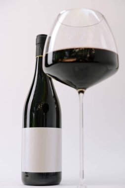 Güzel şekilli bir bardak, basit, işaretlenmemiş bir şişenin yanında zengin kırmızı şarap tutar. Minimalist zemin, şarap gösteriminin inceliğini arttırır..