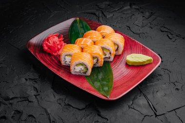 A vibrant platter of sushi presenting salmon rolls and wasabi, complemented by pickled ginger. The dish is set against a dark textured background, highlighting its colors. clipart