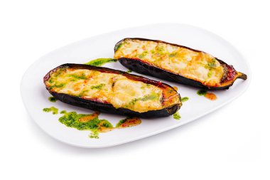 Erimiş peynirle doldurulmuş patlıcanlar canlı yeşil sosla süslenmiş beyaz bir tabakta otururlar. Bu yemek leziz bir lezzet ve doku kombinasyonu sergiliyor..