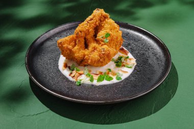 Çok güzel sunulmuş çıtır bir kızarmış yemek, yanında kremalı hindistan cevizi sosu ve taze otlarla süslenmiş ve canlı bir tabakta kızarmış bademle servis edilir..