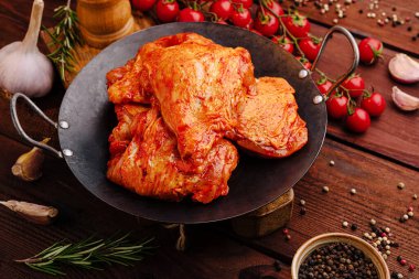 Sulu salamura edilmiş tavuk parçaları canlı kiraz domatesleri ve ahşap bir yüzeyde pişirmeye hazır sarımsakla süslenmiş metal bir kasede oturur..