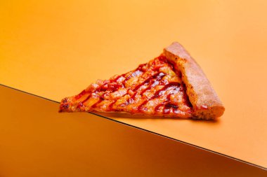 Üçgen şeklinde bir pizza dilimi parlak turuncu bir zemin üzerinde oturmakta, yapışkan peynir ve malzemeler sergilenmektedir. Ekmek kabuğu altın kahverengidir. Canlı bir toplanma ya da atıştırma zamanında paylaşmak için mükemmeldir..