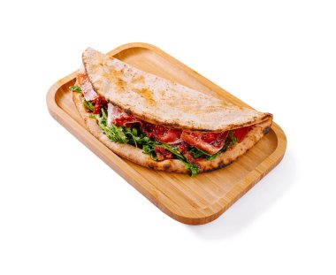 Canlı yeşilliklerle, sulu domateslerle ve erimiş peynirle dolu bir ekmek, ahşap tepside duruyor. Renkli ve iştah açıcı bir yemek sunuyor. Öğle veya akşam yemeği için mükemmel..