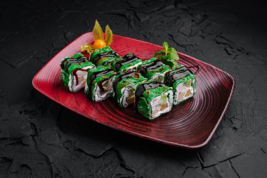 Canlı yeşil malzemelerle yapılan suşi ruloları şık bir kırmızı tabakta dikkatlice düzenlenir. Taze garnitürler bu yemek hazzına biraz zarafet katar, titizlikle hazırlanır..