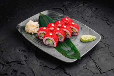 Kırmızı havyar, avokado ve balık sergilenen siyah bir tabakta canlı suşi ruloları zarif bir şekilde düzenlenir. Wasabi ve turşulu zencefil modern bir yemek atmosferine lezzet katar..