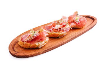 İnce dilim prosciutto ile kaplanmış ve otlarla süslenmiş üç dilim gevrek bruschetta ahşap bir tabakta güzelce düzenlenir. Aperatifler ya da hafif atıştırmalıklar için mükemmel.